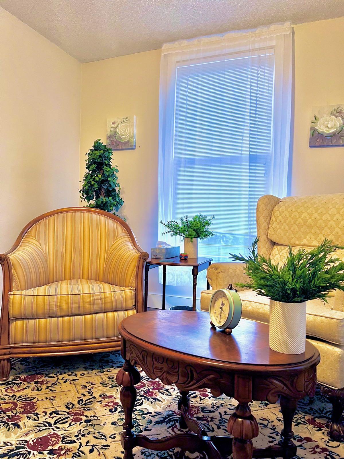 Therapy sitting room with two armchairs, a wooden coffee table, and a window with sheer curtains
